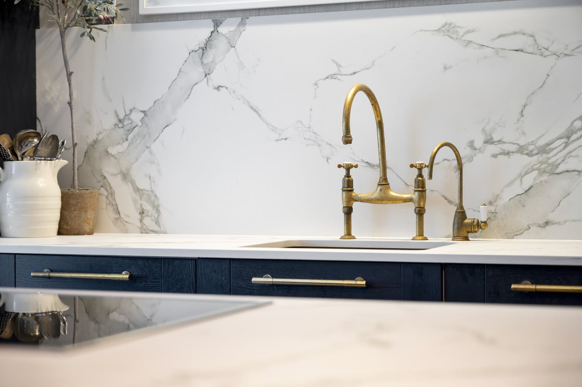 Unlacquered brass bridge tap against a marble splashback