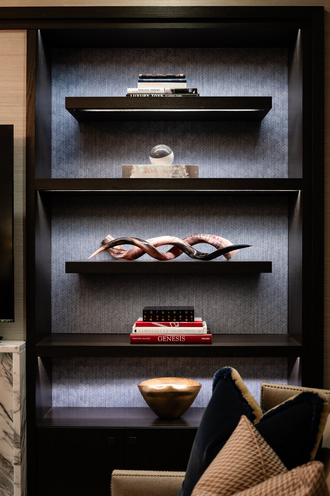 Backlit dark shelving with a twisted horn sculpture and a brass bowl